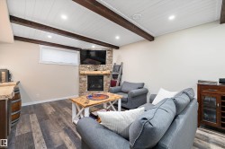 Living area with dark wood-style flooring, a stone fireplace, recessed lighting, and beamed ceiling - 