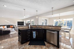 Kitchen with dark cabinets, an island with sink, a textured ceiling, dishwasher, and open floor plan - 