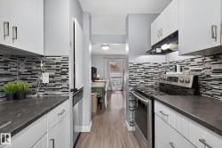 Kitchen featuring stainless steel appliances, white cabinetry, under cabinet range hood, light wood finished floors, and a textured ceiling - 