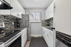Kitchen with stainless steel appliances, ventilation hood, white cabinets, light wood-style floors, and a textured ceiling - 