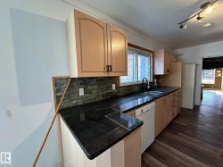 Kitchen featuring decorative backsplash, white dishwasher, a peninsula, dark wood-style flooring, and light brown cabinets - 