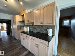 Kitchen featuring decorative backsplash, dark wood-style flooring, dark stone countertops, light brown cabinetry, and wall chimney exhaust hood - 