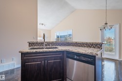 Kitchen with dishwasher, hanging light fixtures, dark wood finished floors, dark brown cabinetry, and light stone counters - 