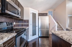 Kitchen featuring appliances with stainless steel finishes, dark wood-style flooring, dark brown cabinetry, backsplash, and light stone counters - 