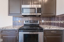 Kitchen with appliances with stainless steel finishes, light stone countertops, decorative backsplash, and dark brown cabinetry - 