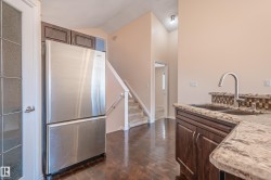 Kitchen with freestanding refrigerator, dark wood-style floors, dark brown cabinetry, light stone counters, and high vaulted ceiling - 