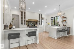 Kitchen featuring a kitchen bar, a peninsula, a chandelier, ornamental molding, and white cabinets - 