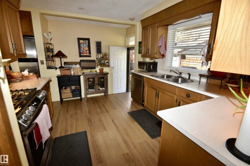 Kitchen featuring light countertops, stainless steel appliances, brown cabinets, light wood finished floors, and a textured ceiling - 13910 101A Avenue, Edmonton, AB - Indoor Photo Showing Kitchen With Double Sink