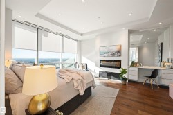 Bedroom featuring built in study area, a raised ceiling, a glass covered fireplace, recessed lighting, and dark wood-style floors - 