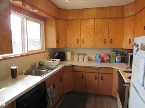 Kitchen featuring white appliances, brown cabinetry, light countertops, and backsplash - 5016 51 Street, Barrhead, AB - Indoor Photo Showing Kitchen With Double Sink