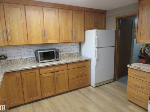 Kitchen with backsplash, brown cabinets, freestanding refrigerator, and stainless steel microwave - 5016 51 Street, Barrhead, AB - Indoor Photo Showing Kitchen