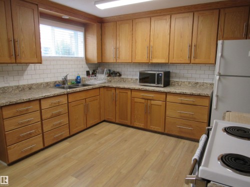 Kitchen with white appliances, light wood-style floors, decorative backsplash, and brown cabinetry - 5016 51 Street, Barrhead, AB - Indoor Photo Showing Kitchen With Double Sink