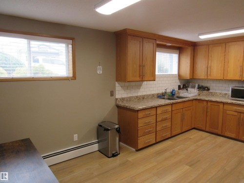 Kitchen with decorative backsplash, a baseboard radiator, brown cabinets, and light wood finished floors - 5016 51 Street, Barrhead, AB - Indoor Photo Showing Kitchen With Double Sink