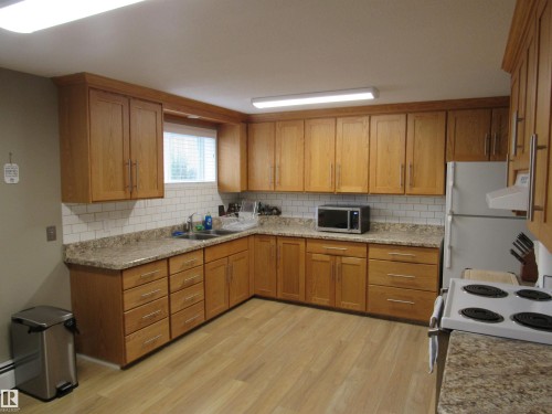 Kitchen with tasteful backsplash, white appliances, light wood-style floors, and brown cabinets - 5016 51 Street, Barrhead, AB - Indoor Photo Showing Kitchen With Double Sink