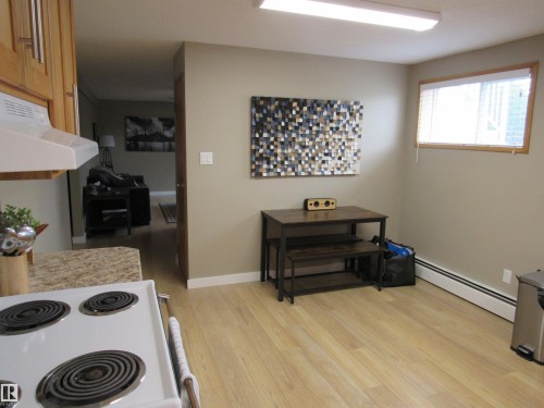 Kitchen with white range with electric stovetop, baseboard heating, light wood-style flooring, and exhaust hood - 5016 51 Street, Barrhead, AB - Indoor
