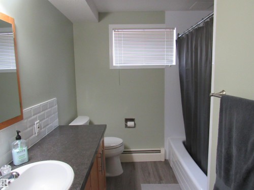Bathroom featuring baseboard heating, dark wood-style floors, vanity, decorative backsplash, and shower / tub combo with curtain - 5016 51 Street, Barrhead, AB - Indoor Photo Showing Bathroom