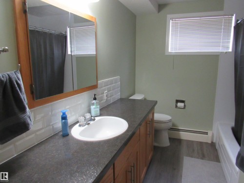 Full bathroom featuring dark wood finished floors, baseboard heating, decorative backsplash, vanity, and a shower with curtain - 5016 51 Street, Barrhead, AB - Indoor Photo Showing Bathroom