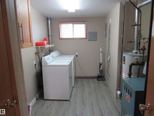 Washroom featuring light wood-style flooring, washing machine and clothes dryer, a heating unit, and water heater - 5016 51 Street, Barrhead, AB - Indoor Photo Showing Laundry Room