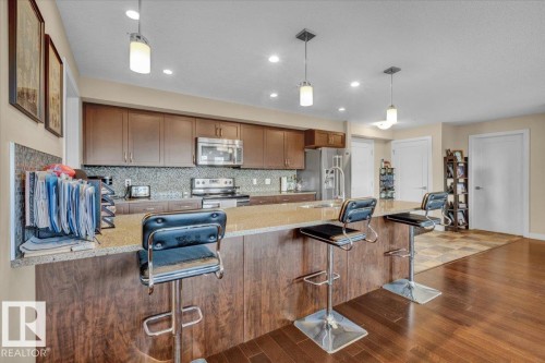 Kitchen with a peninsula, decorative backsplash, light stone countertops, appliances with stainless steel finishes, and recessed lighting - 305 5029 Edgemont Boulevard, Edmonton, AB - Indoor Photo Showing Kitchen
