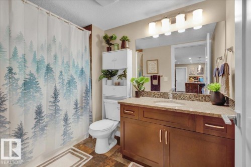 Full bathroom with a shower with shower curtain, vanity, a textured ceiling, and dark stone finish floors - 305 5029 Edgemont Boulevard, Edmonton, AB - Indoor Photo Showing Bathroom