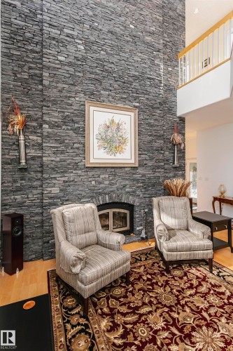 Living area with a glass covered fireplace, light wood-type flooring, and a towering ceiling - 19103 Ellerslie Road Sw, Edmonton, AB - Indoor With Fireplace