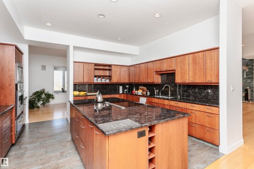 Kitchen with open shelves, decorative backsplash, dark stone counters, an island with sink, and light wood finished floors - 19103 Ellerslie Road Sw, Edmonton, AB - Indoor Photo Showing Kitchen