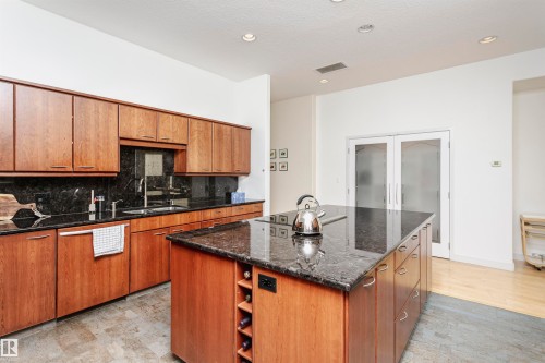 Kitchen featuring decorative backsplash, dark stone countertops, brown cabinetry, a center island, and recessed lighting - 19103 Ellerslie Road Sw, Edmonton, AB - Indoor Photo Showing Kitchen