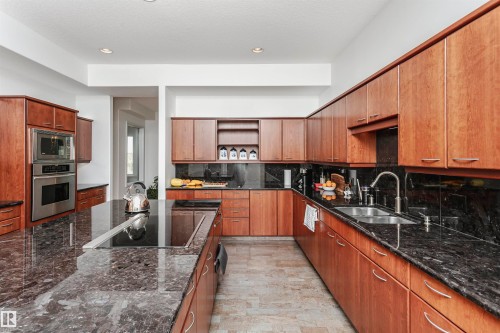 Kitchen with open shelves, dark stone counters, stainless steel appliances, decorative backsplash, and brown cabinetry - 19103 Ellerslie Road Sw, Edmonton, AB - Indoor Photo Showing Kitchen With Double Sink