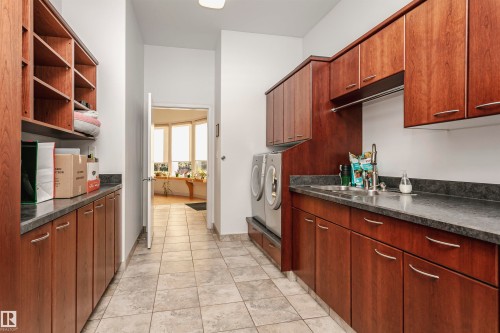 Kitchen with dark countertops, light tile patterned floors, washer and dryer, and open shelves - 19103 Ellerslie Road Sw, Edmonton, AB - Indoor Photo Showing Kitchen