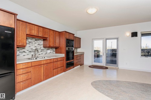Kitchen featuring backsplash, light countertops, black appliances, and brown cabinets - 19103 Ellerslie Road Sw, Edmonton, AB - Indoor Photo Showing Kitchen With Double Sink