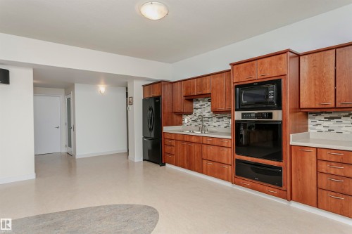 Kitchen with brown cabinets, decorative backsplash, black appliances, a warming drawer, and light stone countertops - 19103 Ellerslie Road Sw, Edmonton, AB - Indoor Photo Showing Kitchen