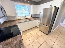 Kitchen with light tile patterned floors, appliances with stainless steel finishes, white cabinets, dark stone counters, and backsplash - 