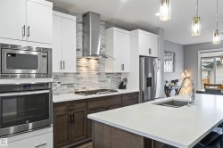 Kitchen featuring decorative backsplash, appliances with stainless steel finishes, pendant lighting, wall chimney range hood, and an island with sink - 