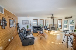 Living room featuring a wood stove, wood walls, light wood-style floors, and ceiling fan - 