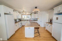 Kitchen with white appliances, backsplash, a kitchen breakfast bar, white cabinets, and light wood-type flooring - 