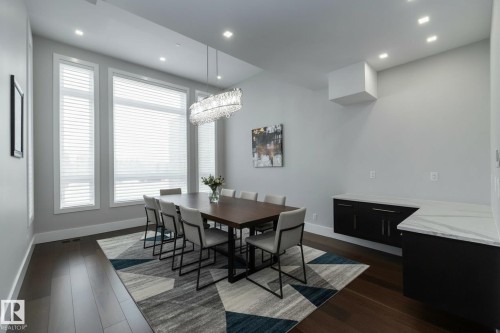 This dining area features rich hardwood flooring, a contemporary light fixture, and a large window arrangement that provides ample natural light - 14 3466 Keswick Boulevard, Edmonton, AB - Indoor Photo Showing Dining Room