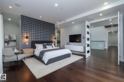 This spacious room features dark hardwood flooring, recessed lighting, and a striking accent wall with a geometric pattern - 