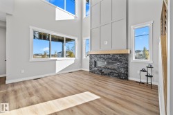 Unfurnished living room featuring a high ceiling, light wood finished floors, and a stone fireplace - 