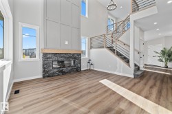 Unfurnished living room featuring a high ceiling, a fireplace, wood finished floors, stairs, and recessed lighting - 