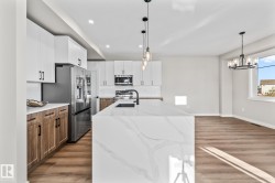 Kitchen with light wood finished floors, white cabinets, light stone counters, stainless steel appliances, and recessed lighting - 