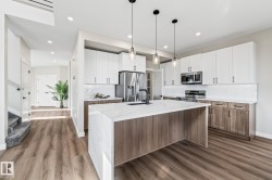 Kitchen with dark wood-style flooring, decorative backsplash, stainless steel appliances, white cabinets, and brown cabinetry - 