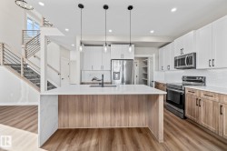 Kitchen featuring backsplash, appliances with stainless steel finishes, white cabinets, light stone counters, and light wood finished floors - 