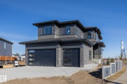 View of front of property featuring an attached garage, stone siding, driveway, and roof with shingles - 