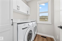 Washroom featuring dark wood-style floors, washer and clothes dryer, and cabinet space - 