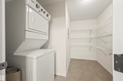 Laundry room with a textured ceiling, stacked washing machine and dryer, and light tile patterned floors - 