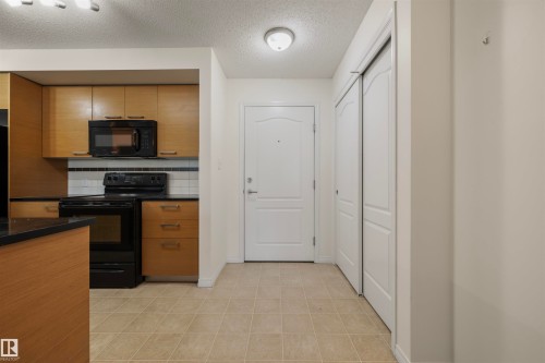 Kitchen with black appliances, decorative backsplash, a textured ceiling, light tile patterned floors, and brown cabinetry - 2209 7343 South Terwillegar Drive, Edmonton, AB - Indoor Photo Showing Kitchen