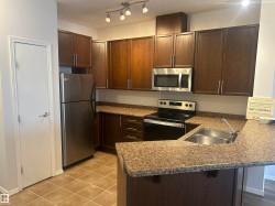 Kitchen featuring stainless steel appliances, dark brown cabinets, a peninsula, a kitchen breakfast bar, and a textured ceiling - 