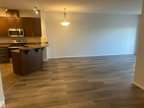 Kitchen with a kitchen bar, appliances with stainless steel finishes, decorative light fixtures, dark stone counters, and a peninsula - 411 4316 139 Avenue, Edmonton, AB - Indoor Photo Showing Kitchen