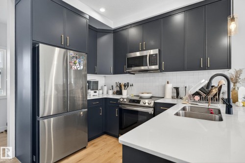 Kitchen with stainless steel appliances, light wood-type flooring, light stone counters, tasteful backsplash, and decorative light fixtures - 382 Crystallina Nera Drive, Edmonton, AB - Indoor Photo Showing Kitchen With Stainless Steel Kitchen With Double Sink With Upgraded Kitchen