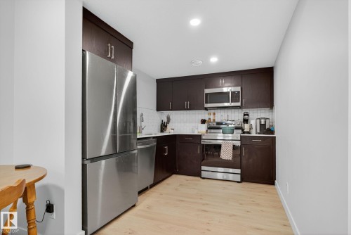 Kitchen with dark brown cabinetry, stainless steel appliances, tasteful backsplash, light wood-type flooring, and recessed lighting - 382 Crystallina Nera Drive, Edmonton, AB - Indoor Photo Showing Kitchen With Stainless Steel Kitchen